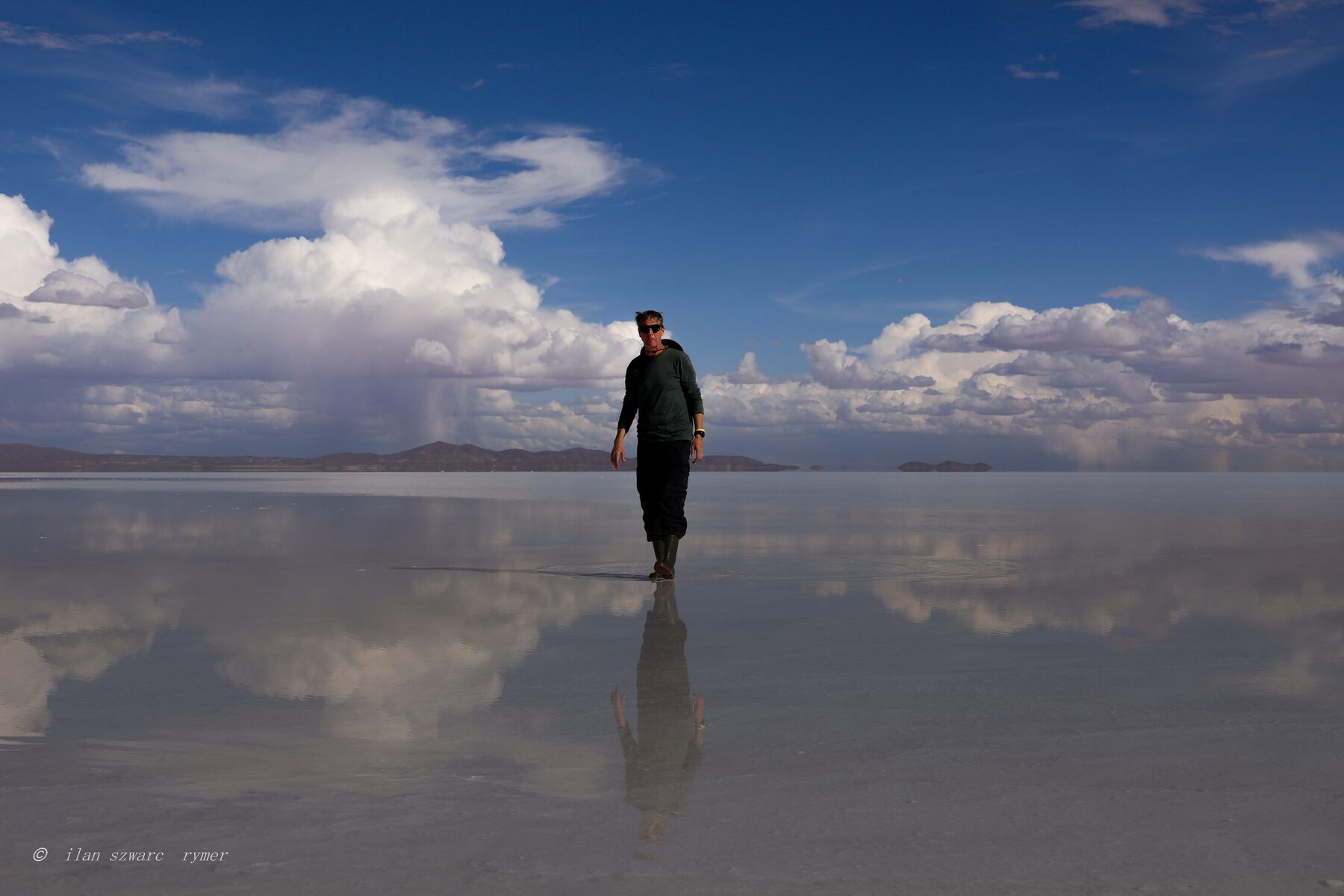 A figure walking across the mirrored Salar de Uyuni salt flat